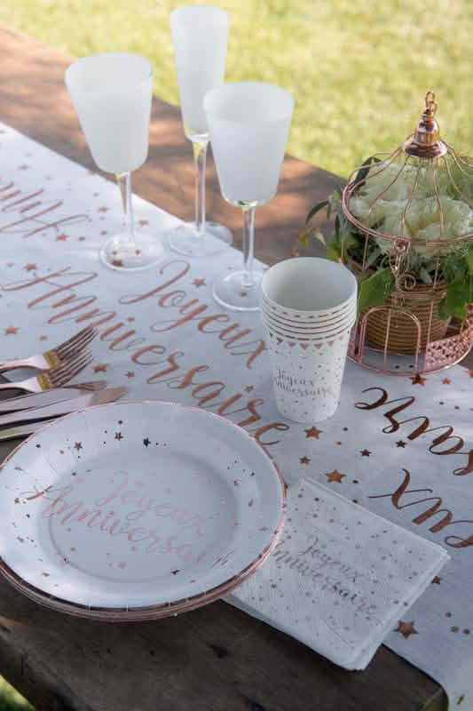 Mise en situation sur table du gobelet en carton Joyeux anniversaire rose gold à étoiles