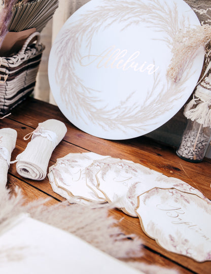 Mise en scène sur table des serviettes en papier pampas et fleurs de coton pour baptême dorées