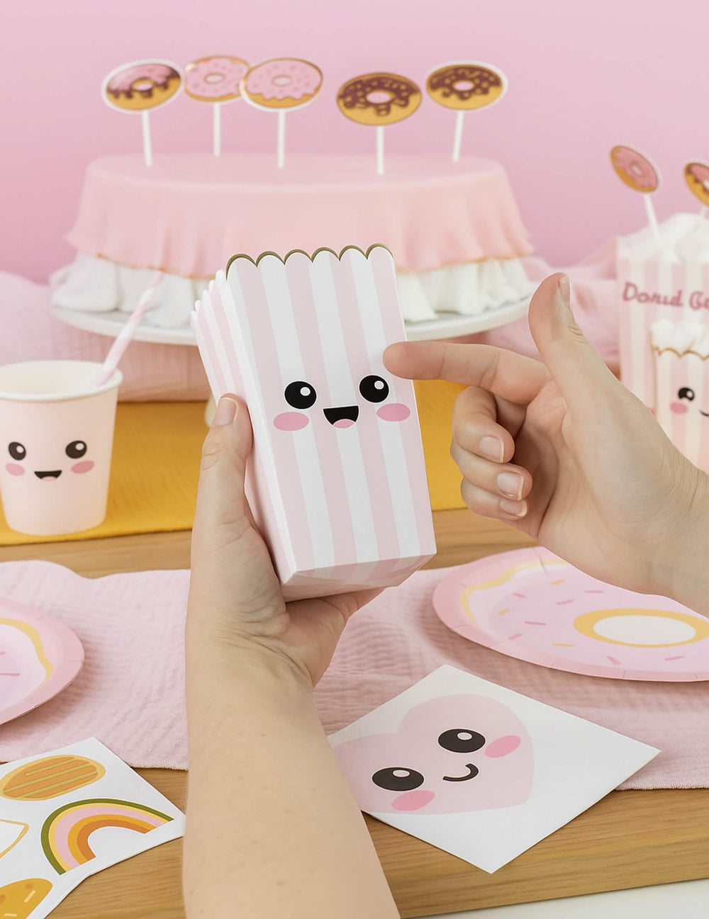 Détail du sticker visage sur les boîtes à pop corn à rayures pour fête rose pastel et blanc avec bordure dorée