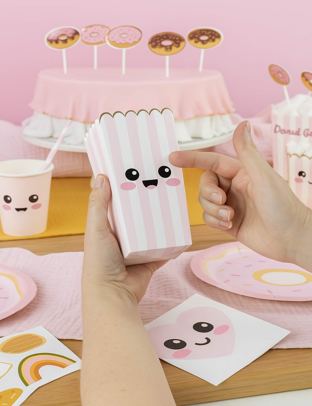 Détail du sticker visage sur les boîtes à pop corn à rayures pour fête rose pastel et blanc avec bordure dorée