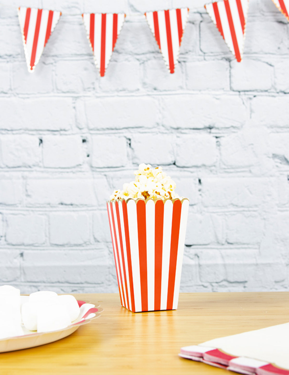 Mise en situation sur une table décorée des boîtes à popcorn à rayures pour fête rouges et blanches avec liseré doré