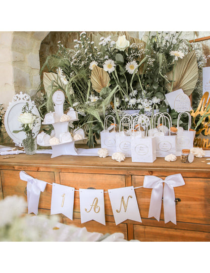 Mise en scène sur un buffet de la guirlande 1 an pour anniversaire blanche et dorée avec nœuds satinés
