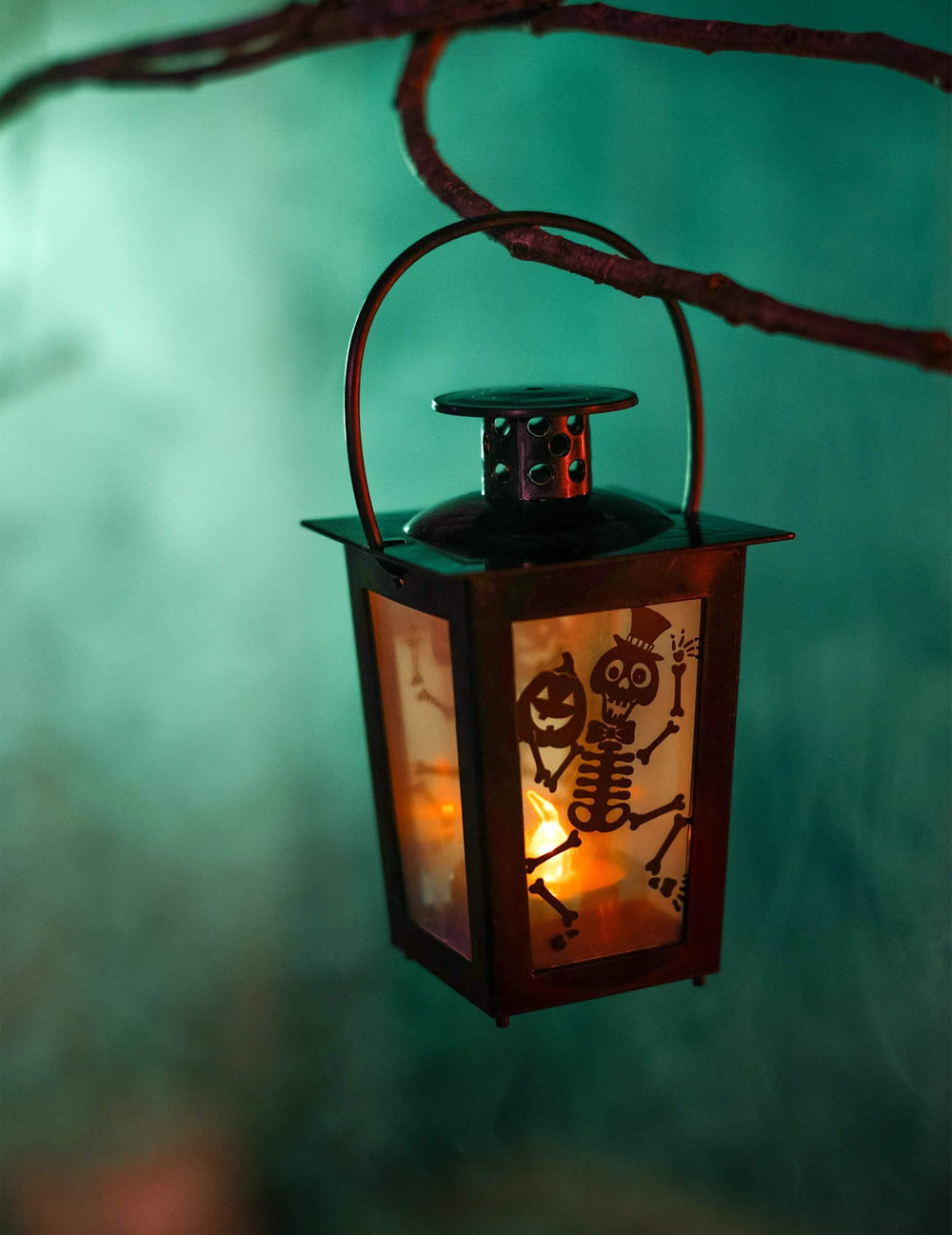 Detail na zavěšenou lucernu visící na větvi svítícího halloweenového lampionu s kostlivcem a dýní